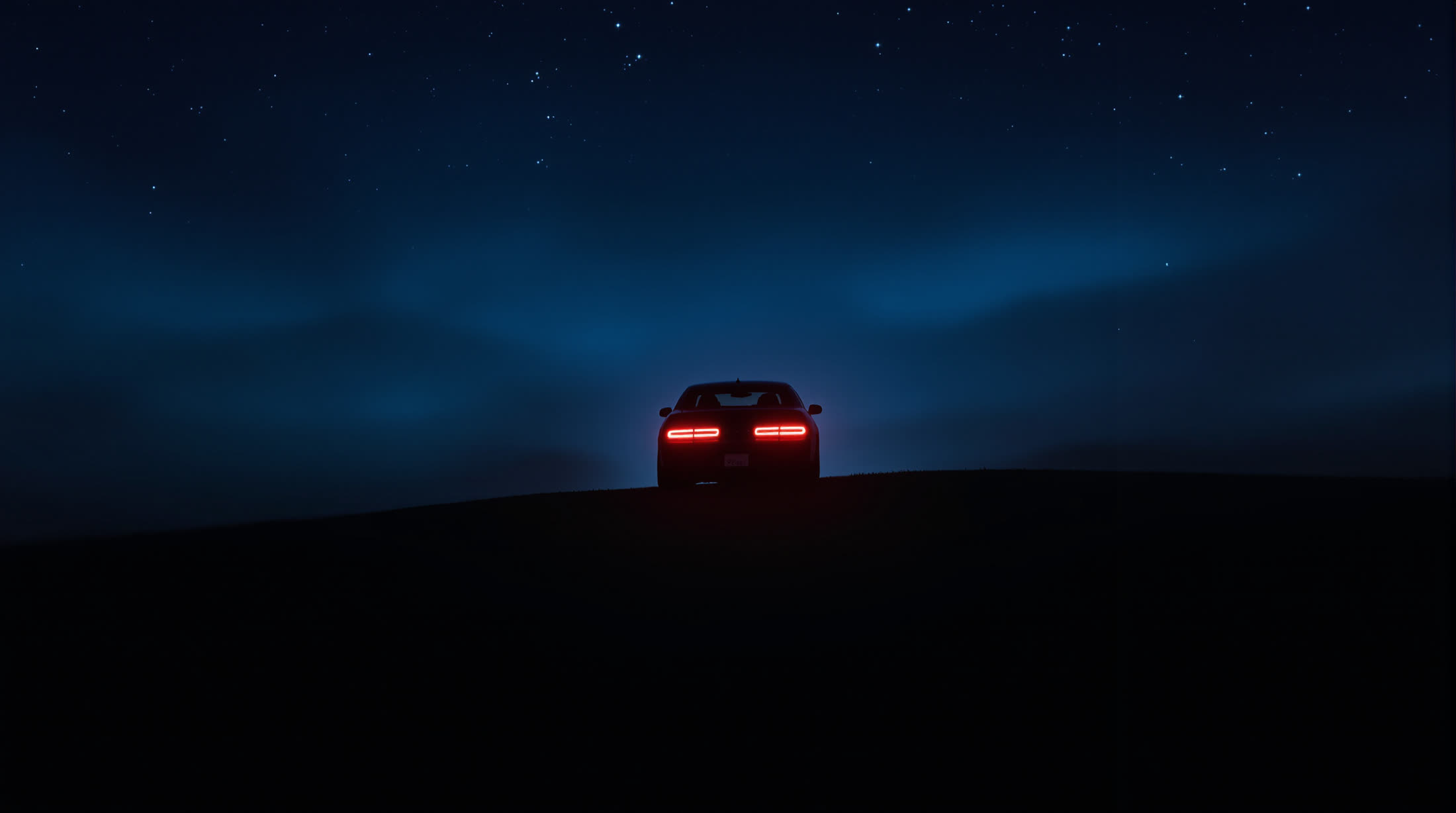 Rear silhouette cresting a ridge at night with only the tail lights lit.